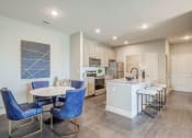 Thumbnail 6 of 28 - one bedroom kitchen with woodgrain light cabinets, stainless steel appliances, granite countertops, kitchen table with blue leather chairs, 6-panel white doors, woodlike plank flooring, and laundry room off the kitchen