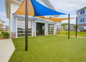 Thumbnail 14 of 28 - plush green grass yoga lawn outside the gym with rolling garage doors open to machines and free weights on the inside.