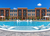 Thumbnail 11 of 23 - A large swimming pool in front of a building with lounge chairs around it.