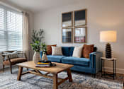 Thumbnail 2 of 14 - A living room with a blue couch, a wooden coffee table, and a lamp.