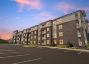 Thumbnail 8 of 20 - A large apartment building with a parking lot in front.