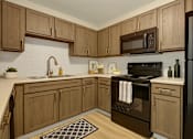 Thumbnail 2 of 16 - A kitchen with wooden cabinets and black appliances.