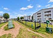 Thumbnail 15 of 22 - Fenced dog park with an agility ramp and pet waste station at Canterbury Apartments in Myrtle Beach, SC.