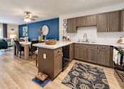 Thumbnail 1 of 22 - Kitchen with gray cabinets, black appliances and an adjoining furnished living area at Canterbury Apartments in Myrtle Beach, SC.