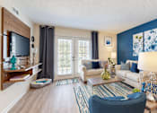 Thumbnail 3 of 22 - Furnished living room with a blue accent wall, cream seating and French doors at Canterbury Apartments in Myrtle Beach, SC.