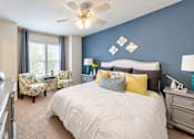 Thumbnail 4 of 22 - Furnished bedroom with a white upholstered headboard, blue accent wall and window seating at Canterbury Apartments in Myrtle Beach, SC.