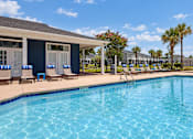 Thumbnail 10 of 22 - Swimming pool beside the main office, with lounge chairs and palm trees at Canterbury Apartments in Myrtle Beach, SC.