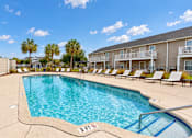 Thumbnail 9 of 22 - Outdoor swimming pool with entry steps, lounge chairs and palm trees at Canterbury Apartments in Myrtle Beach, SC.