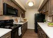 Thumbnail 2 of 18 - A black refrigerator stands in a kitchen with wooden cabinets and a black stove.