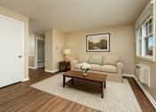 Thumbnail 6 of 18 - A living room with a couch, coffee table, and a painting on the wall.