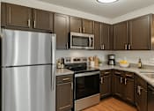 Thumbnail 1 of 15 - A kitchen with a stainless steel refrigerator and brown cabinets.