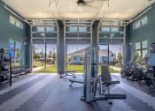 Thumbnail 7 of 28 - brand new fitness center features free weights, medicine balls and slam balls. There are three garage doors opening to to the plush green yoga lawn. Bikes and other machines are also present. The ceiling has a large fan and the walls are a calming tone of greenish blue.