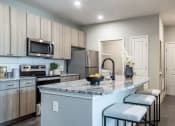 Thumbnail 10 of 28 - Model kitchen with granite countertops featuring a grey and white marble effect. there are stainless steel appliances including microwave, stove and fridge. The gooseneck sink faucet is black.  the cabinets are light woodgrain and the flooring is a wood-like plank.