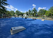 Thumbnail 9 of 17 - A playground with a blue surface and a slide in the foreground.