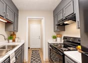 Thumbnail 8 of 15 - Galley kitchen with gray cabinets, black appliances, double sink, and white countertops at Madison Park Apartments & Townhomes.
