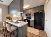 Thumbnail 10 of 15 - Apartment kitchen with gray cabinetry, breakfast peninsula, black appliances, and wood-style flooring at Madison Park in Birmingham, AL.