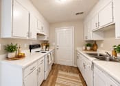 Thumbnail 2 of 15 - Galley-style apartment kitchen with white cabinets, double sink, and wood-style flooring at Madison Park Apartments & Townhomes.