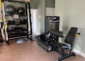 Thumbnail 17 of 24 - A gym with a weight bench, a squat rack, and a wall-mounted pull up bar.