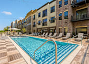 Thumbnail 1 of 19 - A pool surrounded by lounge chairs in front of a building.