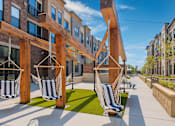 Thumbnail 9 of 19 - A wooden pergola with hanging chairs is in front of a building.