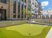 Thumbnail 12 of 19 - A small putting green is surrounded by a brick building.