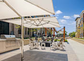Thumbnail 8 of 19 - A patio with a grill and chairs under a white umbrella.