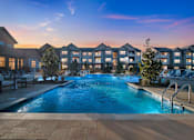 Thumbnail 3 of 25 - A swimming pool in front of apartment buildings at dusk.