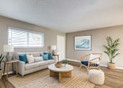 Thumbnail 3 of 16 - A living room with a white couch, a wooden coffee table, and a painting on the wall.