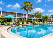 Thumbnail 19 of 24 - Swimming pool with lounge chairs, turquoise umbrellas and palm trees at Waterchase Apartments in Largo, FL.