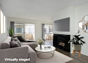 Thumbnail 8 of 19 - A living room with a grey couch, a black fireplace, and a television mounted on the wall.