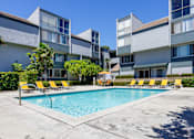 Thumbnail 22 of 45 - a swimming pool with yellow chairs in front of an apartment building