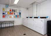 Thumbnail 5 of 19 - a laundry room with four washers and dryers and a table with a shelf
