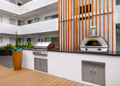 Thumbnail 34 of 63 - A modern outdoor kitchen with a grill and a potted plant.