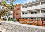 Thumbnail 2 of 63 - A modern building with a white and brown facade is surrounded by a gravel area and a wooden fence.
