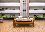 Thumbnail 41 of 63 - A wooden bench with two vases on it in front of a building.