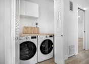 Thumbnail 58 of 63 - A white laundry room with two washing machines and a wooden board on top of the dryer.