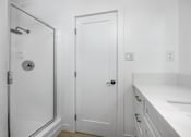 Thumbnail 60 of 63 - A white bathroom with a door, a shower, and a sink.