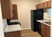 Thumbnail 6 of 6 - A kitchen with a black refrigerator and wooden cabinets.
