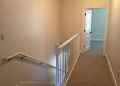 Thumbnail 14 of 22 - A hallway with a carpeted floor and white railings.