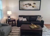 Thumbnail 10 of 22 - A living room with a grey couch, a striped armchair, a wooden coffee table, and a painting on the wall.