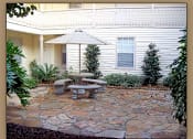 Thumbnail 3 of 7 - A patio with a table and chairs is surrounded by plants.
