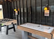 Thumbnail 12 of 24 - A shuffleboard table is in a room with a dark wood wall and a chess table.