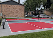 Thumbnail 15 of 24 - A red and white basketball court in front of a brick building.