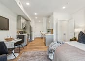 Thumbnail 20 of 57 - A modern bedroom with a large bed and a kitchen area in the background.