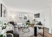 Thumbnail 1 of 15 - A living room with a grey couch, a coffee table, and a television.