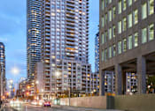 Thumbnail 3 of 24 - A tall building with a curved top stands next to a shorter building with a grid-like facade.