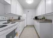 Thumbnail 6 of 12 - A white kitchen with a stove and a refrigerator.