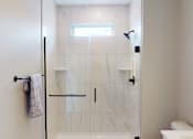 Thumbnail 12 of 15 - A white bathroom with a glass shower door and a towel rack.