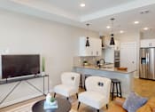 Thumbnail 6 of 15 - A modern living room with a television, two chairs, and a coffee table.