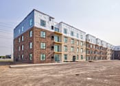 Thumbnail 10 of 25 - A row of multi-story apartment buildings with a parking lot in front.